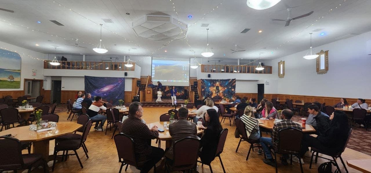 Olha Vozna speaking in a community hall in Lethbridge while guests listen from round tables